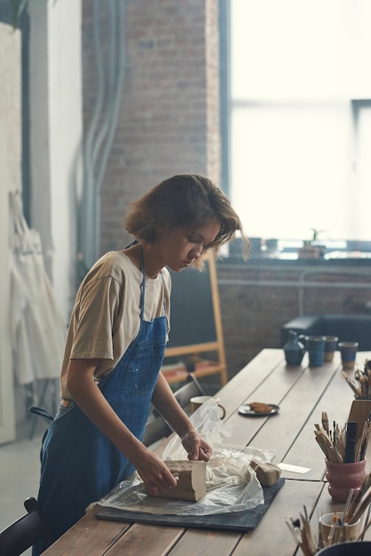 Young female master of pottery working with clay by table