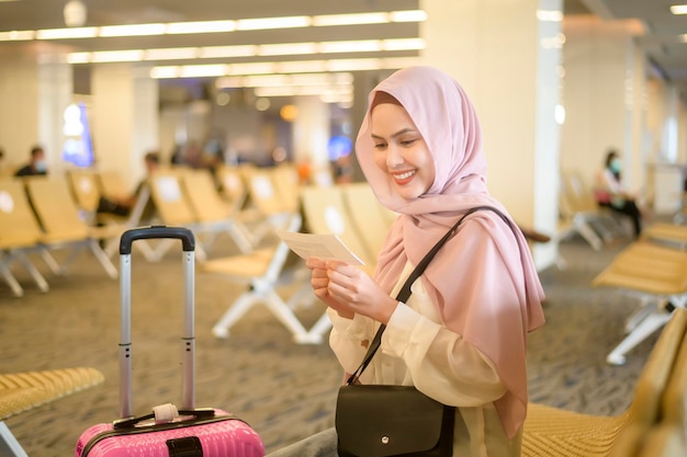 国際空港でスーツケースを運ぶ若い女性のイスラム教徒の旅行者