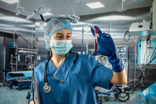 Молодая женщина-медсестра-ученый смотрит на пробирку с кровью в операционной в больнице