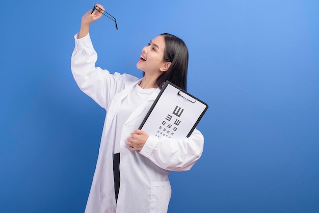 Молодая женщина-офтальмолог в очках держит диаграмму зрения на синем фоне студии, концепция здравоохранения