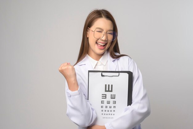 Young female ophthalmologist with glasses holding eye chart over blue background