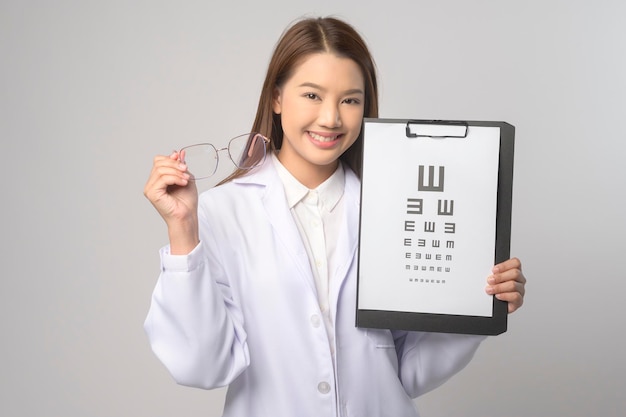 Young female ophthalmologist with glasses holding eye chart over blue background