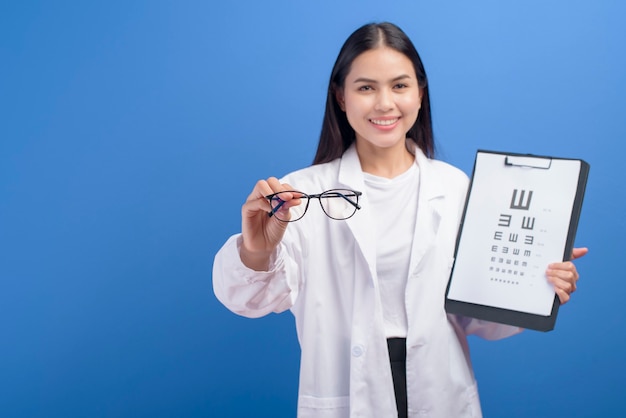 A young female ophthalmologist with glasses holding eye chart over blue , healthcare concept