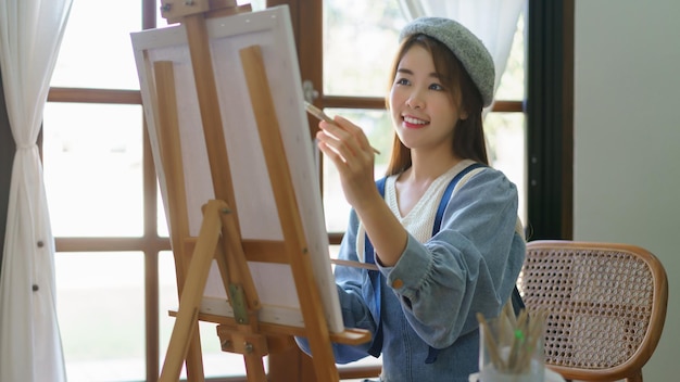 젊은 여성 화가는 홈 스튜디오에서 즐기면서 캔버스에 그림을 그리고 그림을 그립니다.