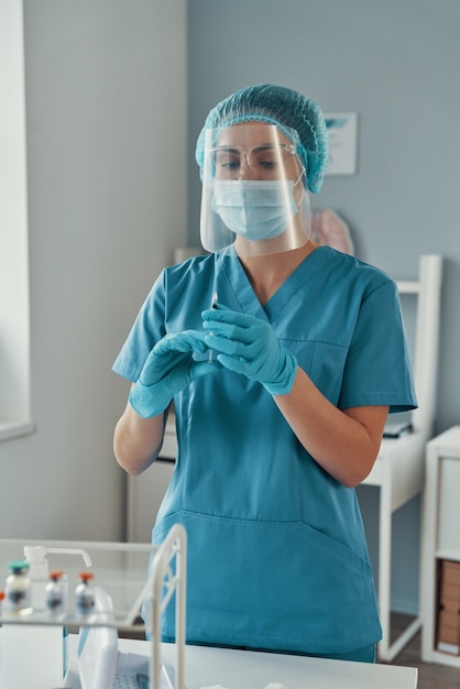 Young female paramedic in protective workwear holding a Covid-19 vaccine while working in the hospital