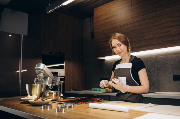 Young female pastry chef pours liquid mousse into a mold Preparation of cake dessert in a professional kitchen