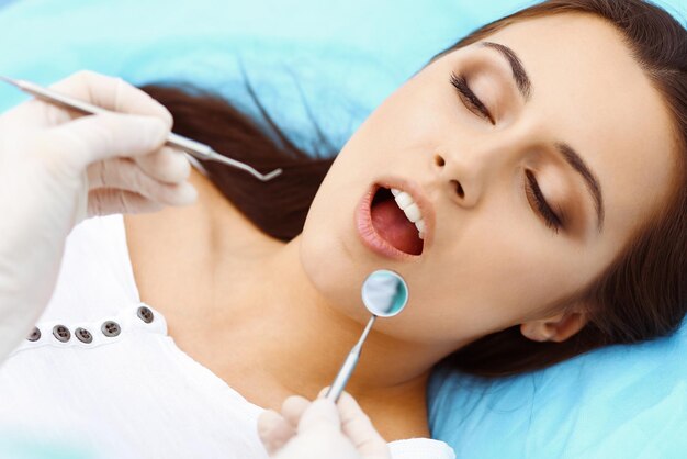 Young female patient visiting dentist office.beautiful woman\
with healthy straight white teeth sitting at dental chair with open\
mouth during oral checkup while doctor working at teeth. dental\
clinic,