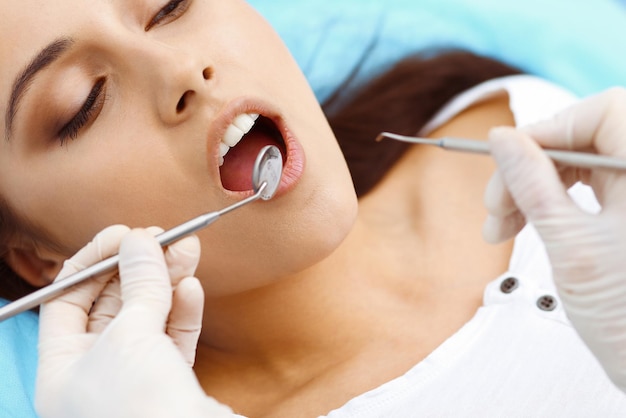 Young female patient visiting dentist office.beautiful woman
with healthy straight white teeth sitting at dental chair with open
mouth during oral checkup while doctor working at teeth. dental
clinic,