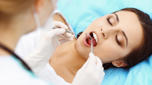 Photo young female patient visiting dentist officebeautiful woman with healthy straight white teeth sitting at dental chair with open mouth during oral checkup while doctor working at teeth