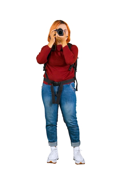 Foto giovane fotografo femminile in abiti invernali casual guardando il mirino scattando foto isolate su sfondo bianco