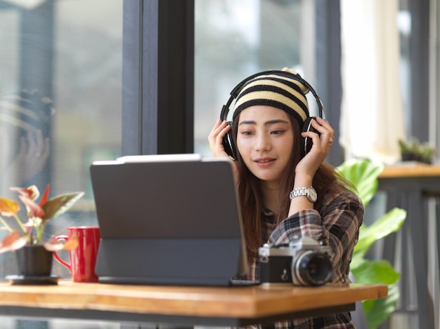 Young female photographer listening to the music through headphones while taking a rest from work