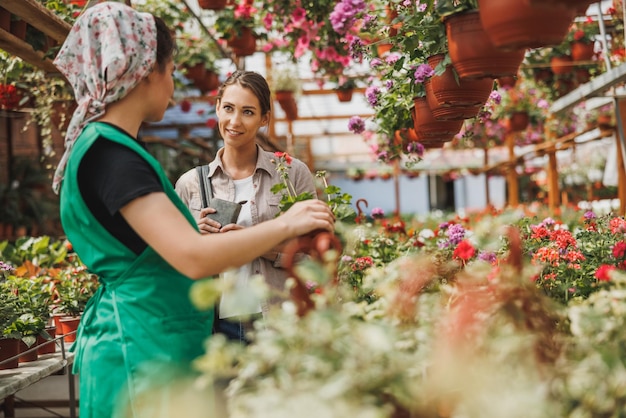 젊은 여성 식물 보육 자원 봉사자는 꽃을 선택하고 구매하는 젊은 여성을 돕습니다.