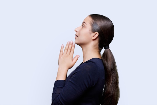 Young female pleading holding hands in prayer on white background profile view