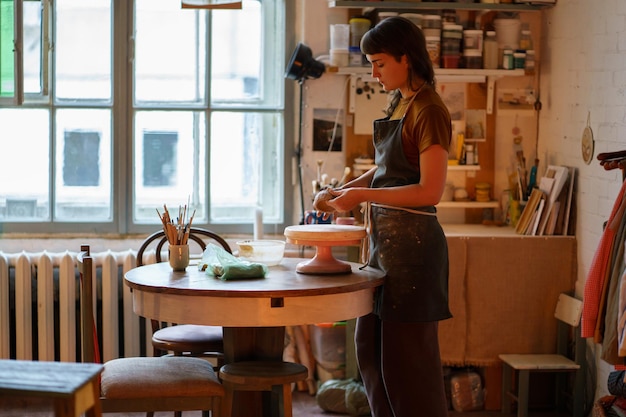 Young female potter maker work with clay on pottery wheel in creative space or professional studio