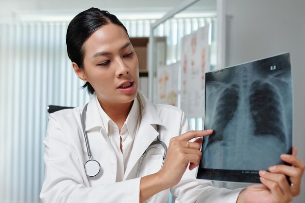 Young female radiologist in lab coat commenting lung xray to patient