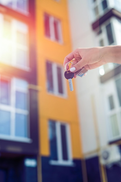 Photo young female realtor smiling confidently holding the key to the new house near the new house the concept of selling a house