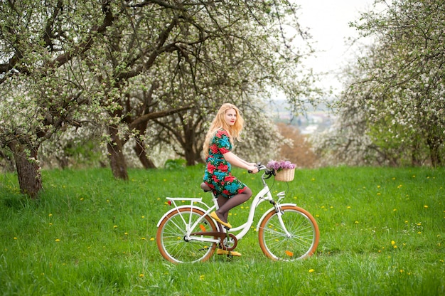 バスケットの花を持つヴィンテージの白い自転車に乗る若い女性