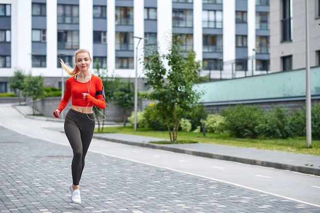 Young female runner in hoody is jogging in the city street.