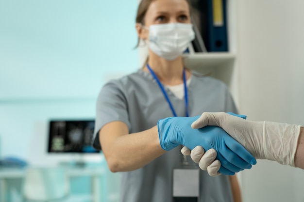 Young female scientific laboratory worker in protective workwear shaking hand of male colleague after finishing work over new effective vaccine