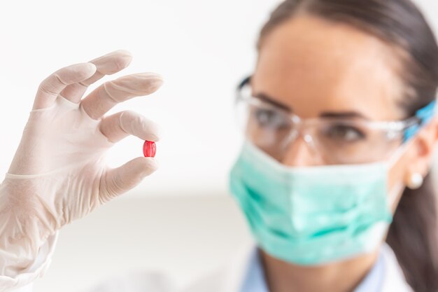 Young female scientist holding a red pill - close-up.