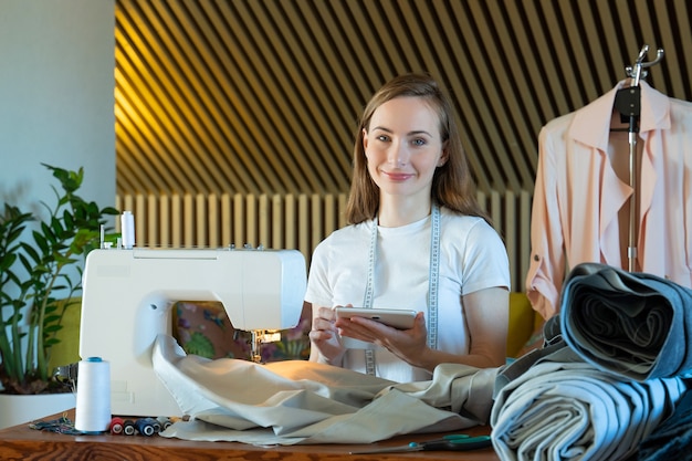 Young female seamstress makes notes about clothing measurements on a notebook in a sewing workshop