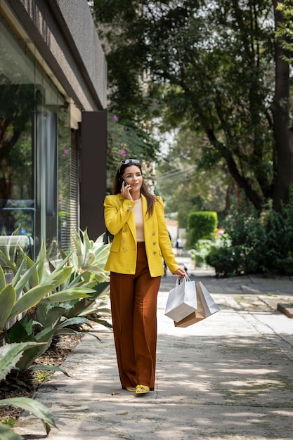 Young female shopping executive carrying her bags while talking on cell phone