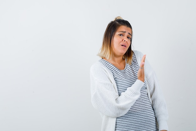 Young female showing something in t-shirt, cardigan and looking upset. front view.