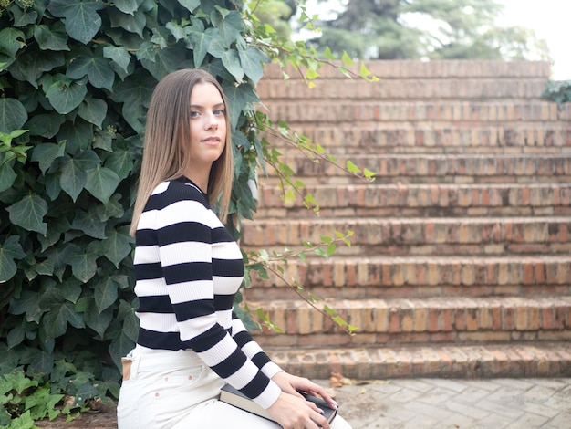 Young female sitting on bench near staircase with book