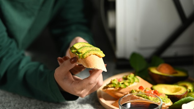 Young female sitting in kitchen and eating healthy avocado toasts