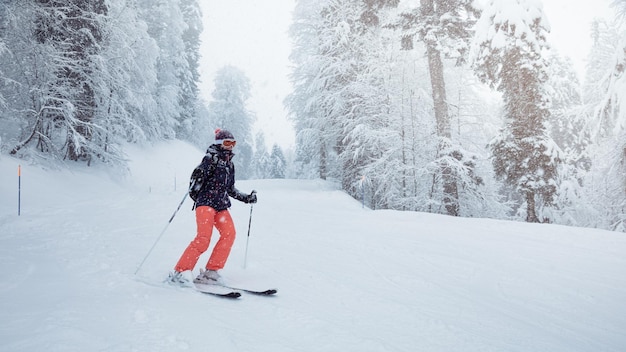 降雪の下で斜面を滑り落ちる若い女性スキーヤー