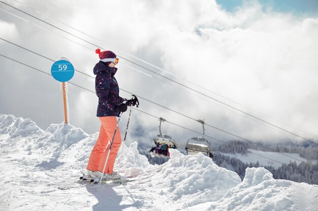 スキー場の山に立っている若い女性スキーヤーと背景のチェアリフトソチクラスナヤポリアナロシア