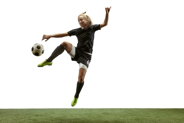 Young female soccer or football player with long hair in sportwear and boots kicking ball for the goal in jump on white background. Concept of healthy lifestyle, professional sport, motion, movement.