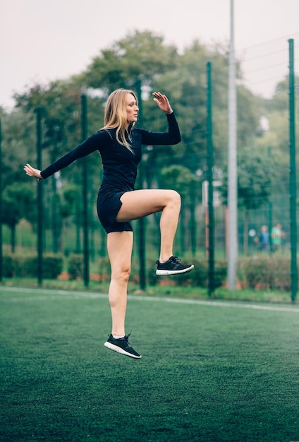 Young female in sportswear lunges and jumps on sports ground Side view