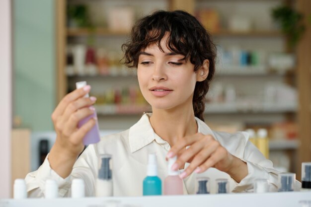 Young female staff of cosmetic supermarket looking through new assortment