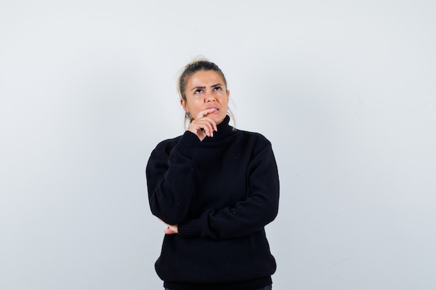 Young female standing in thinking pose in black turtleneck sweater and looking pensive. front view.