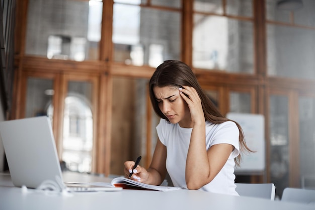 若い女性のスタートアップの所有者は、広々としたカフェのコワーキングに座ってビジネスを速く成長させるためのアイデアをブレインストーミングします