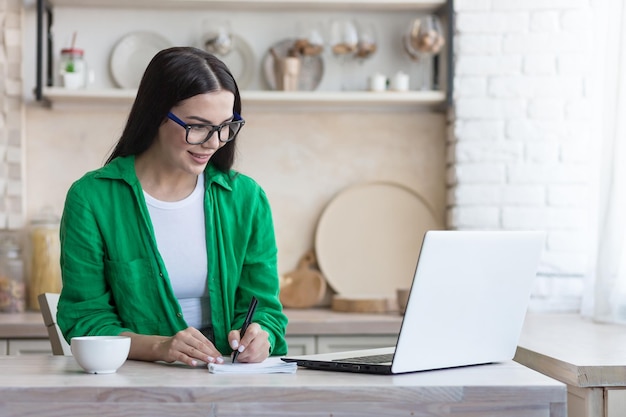 A young female student a freelancer studies works online remotely at home from a laptop he sits at