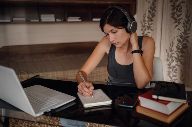 Young female student in headphones using laptop communicates on internet with teachers