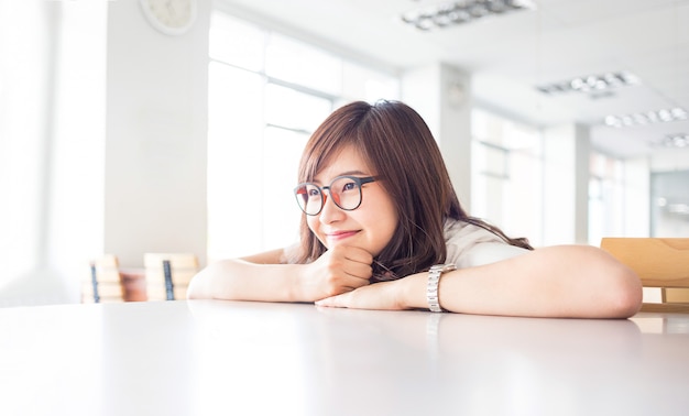 Young female student is smiling with empty copy space on desk in library in campus of university