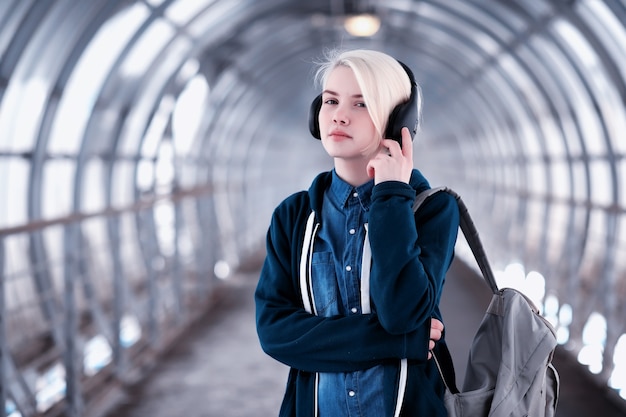 Young female student listening to music in big headphones in the subway tunnel