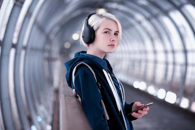 Молодая студентка слушает музыку в больших наушниках в туннеле метро