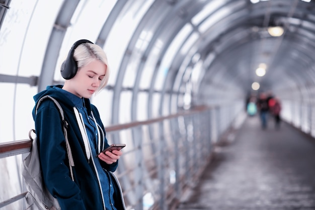 young female student listening to music in big headphones in the subway tunnel