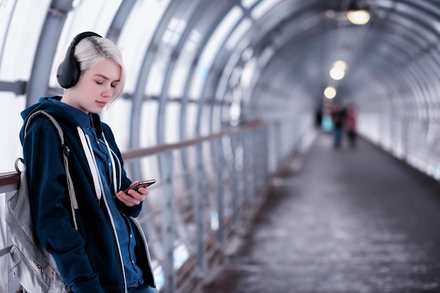 young female student listening to music in big headphones in the subway tunnel
