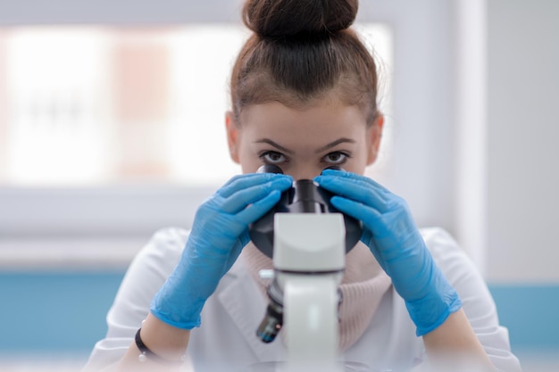 Young female student scientist looking through a microscope while doing some research in the laboratory