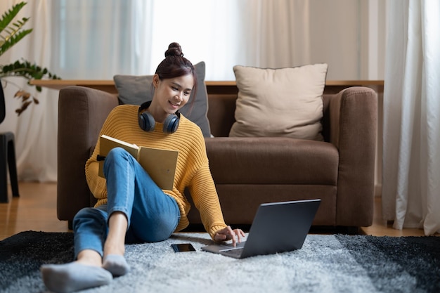 Foto una giovane studentessa seduta sul pavimento con cuffie e computer portatile per studiare prendendo nota dell'istruzione online