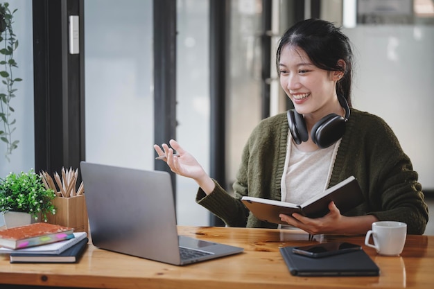 A young female student sitting at the table using headphones and laptop when studying