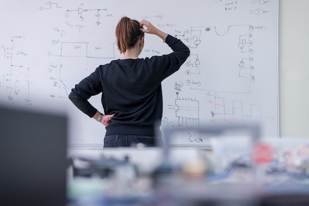 Young female student standing and writing on white chalkboard in a classroom