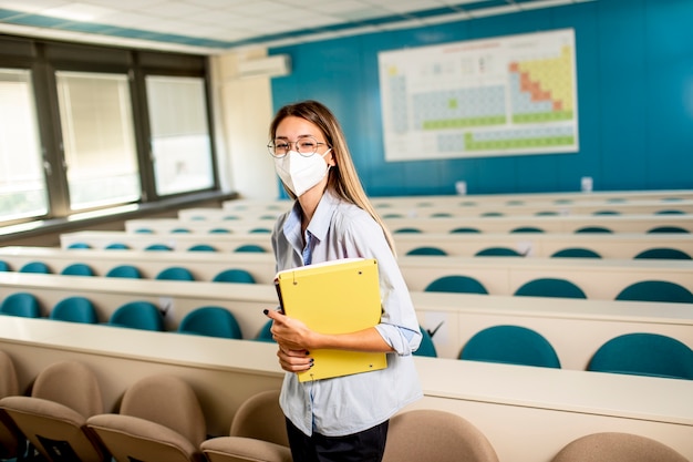 Young female student wearing face protective medical mask for virus protection standing at lecture hall