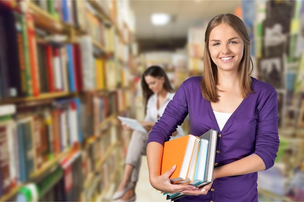 Young female student with stack of books on blurred library background