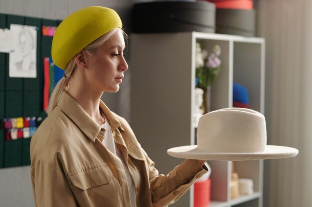 Young female stylist or owner of new fashion brand holding white hat